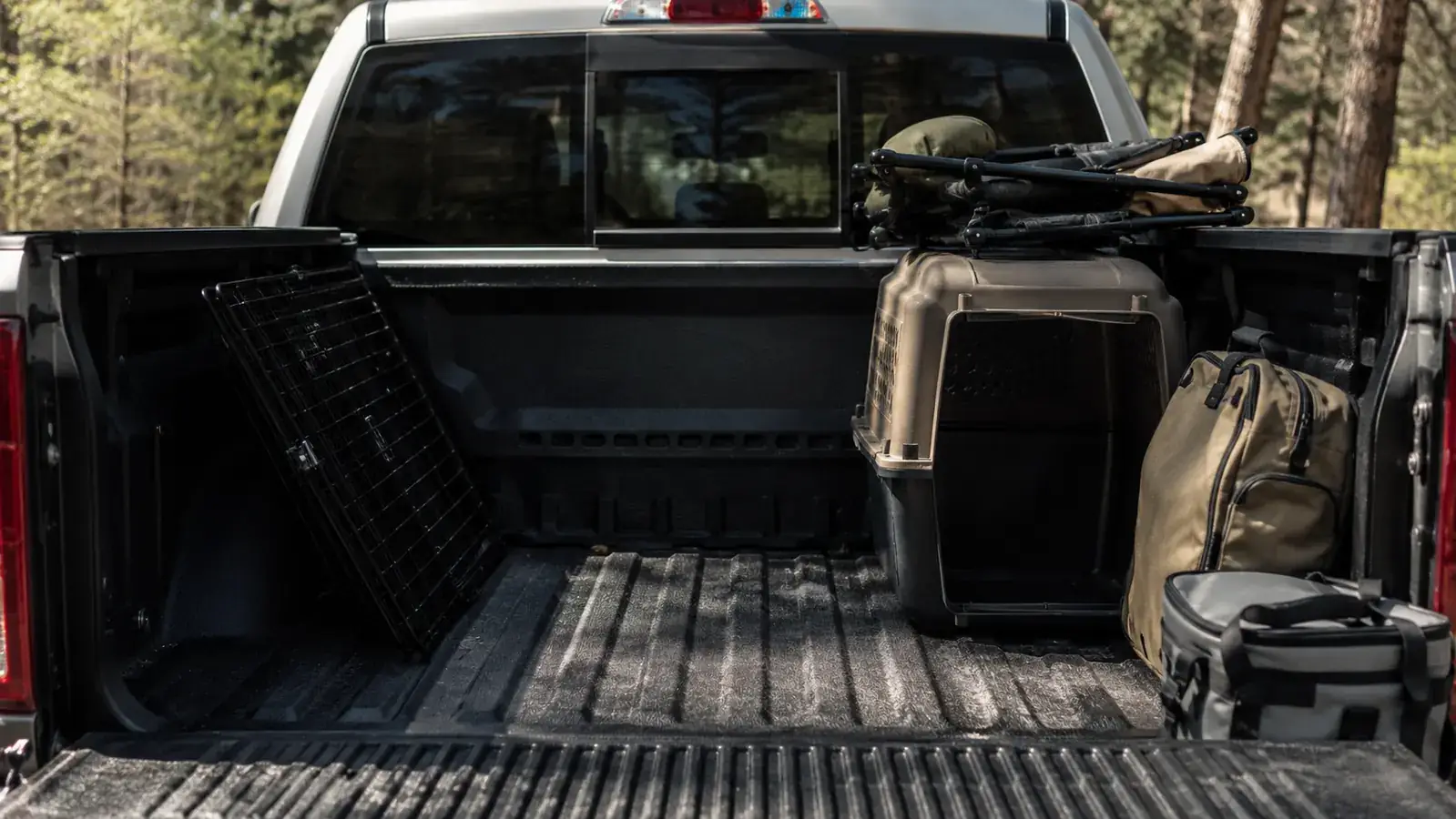 Wire crate folded flat against the cab wall beside a plastic kennel stacked with camp chairs and gear in a truck bed